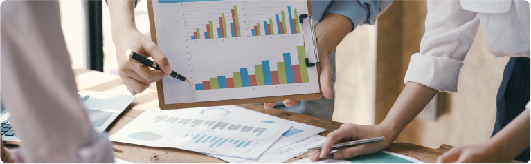 Hands pointing at business bar charts on clipboard during team discussion