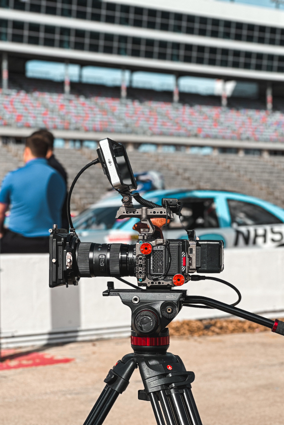 Mounted video camera filming at race track with blurred car and crew in background