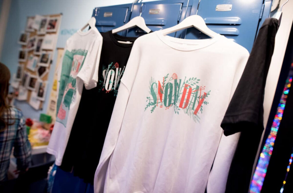 A close-up of several t-shirts hanging on a rack in front of blue lockers.