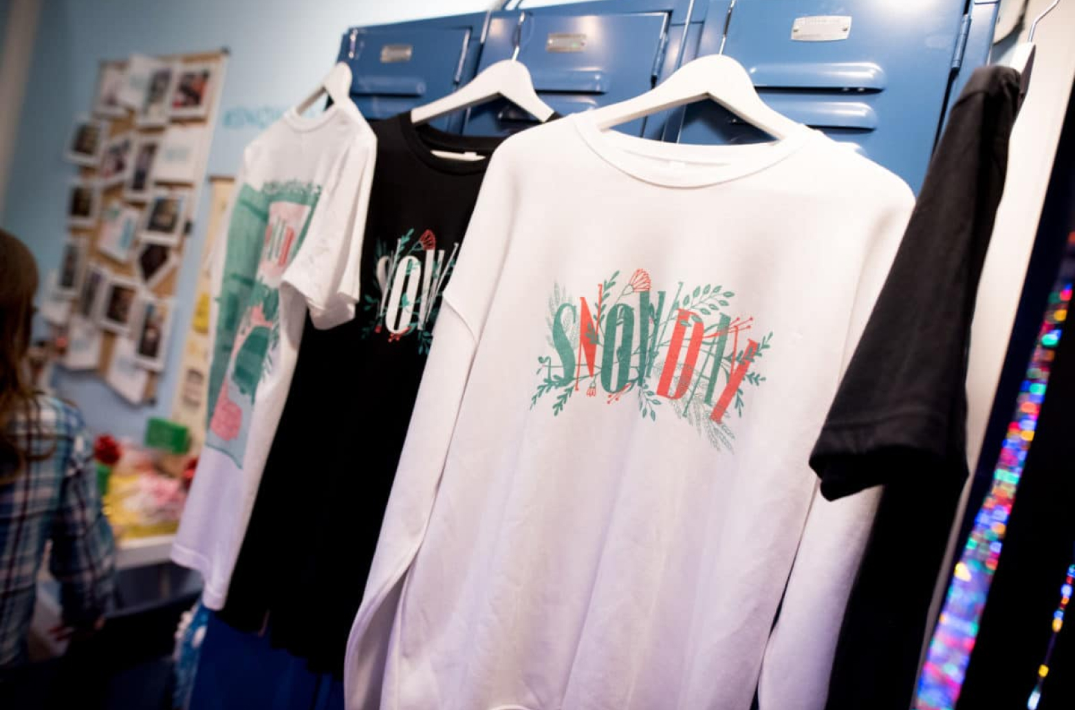 A close-up of several t-shirts hanging on a rack in front of blue lockers.