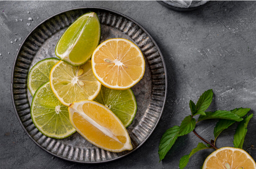A top-down view of sliced limes and lemons on a dark, rustic plate with a mint sprig.