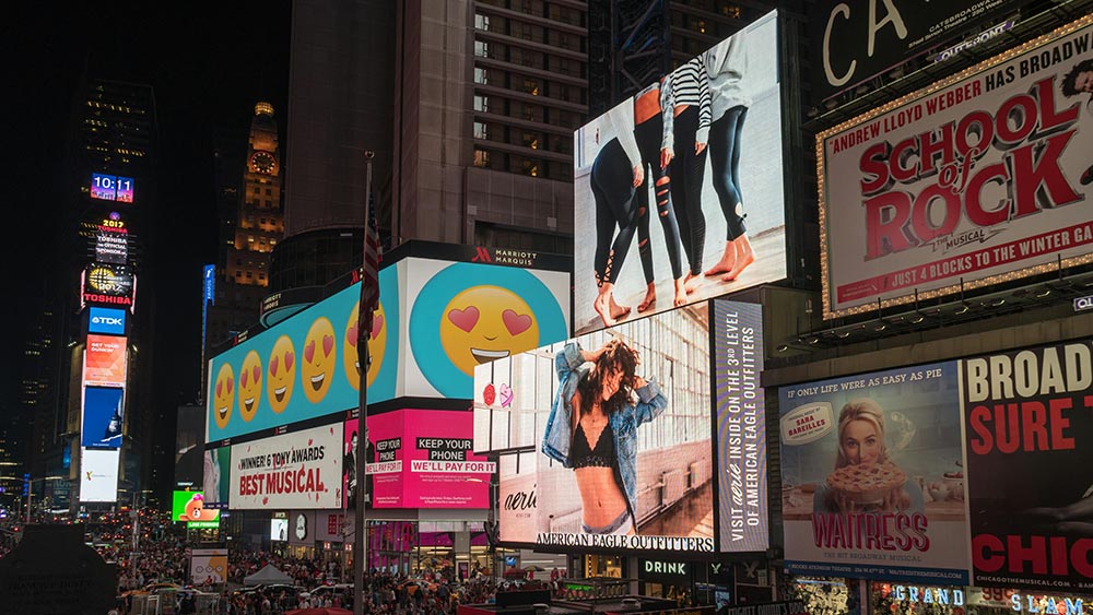 Digital billboards in Times Square showcasing fashion, musicals, and emoji-themed ads
