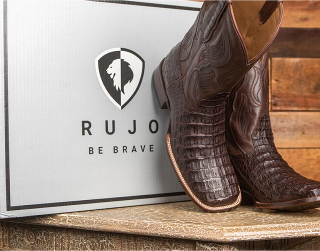 Brown leather cowboy boots displayed in front of RUJO Be Brave logo box